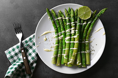 Fresh asparagus with lime on white plate with checkered cotton serviette on grey table