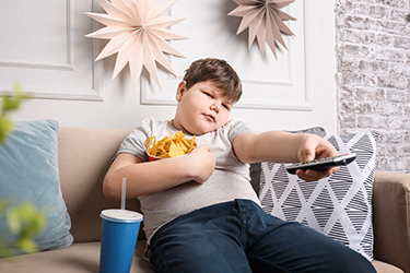 Overweight boy watching TV with snacks indoors