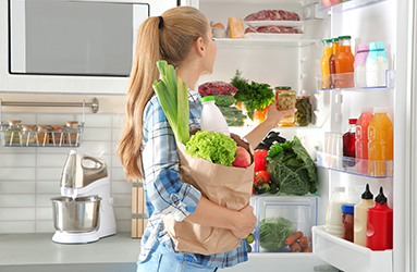 Woman putting products into refrigerator in kitchen Woman putting products into refrigerator in kitchen