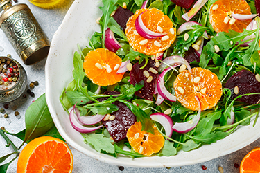 gourmet salad of arugula, baked beetroot, tangerines and red onions with spices and pine nuts in a white dish. Olive oil and ingredients on a grey surface. Selective focus gourmet salad of arugula, baked beetroot, tangerines and red onions with spices and pine nuts in a white dish. Olive oil and ingredients on a grey surface. Selective focus