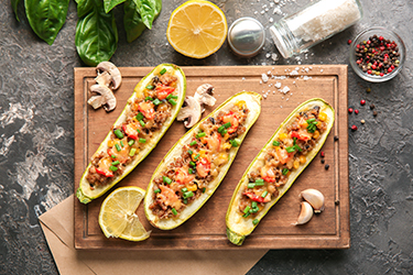 Board with meat stuffed zucchini boats and spices on grunge table