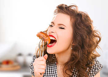 hungry young woman eating meat on fork in kitchen