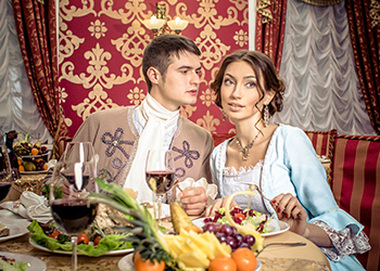 young man in a historic jacket and girl in vintage dress sitting at the richly laid table in a restaurant. Elegant vintage couple in restaurant. Retro couple portrait. Romantic Beauty.Vintage Styled