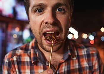 Caucasian young male eating cricket at night market in Thailand. Caucasian young male eating cricket at night market in Thailand.