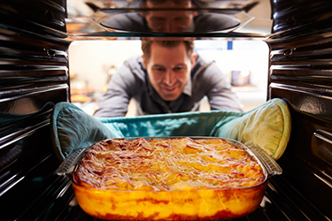 Man Taking Cooked Dish Of Lasagne Out Of The Oven