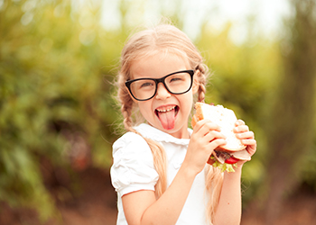 Funny kid girl eating sandwich outdoors. Having fun. Looking at camera. Posing over nature background. Healthy food. Childhood. Funny kid girl eating sandwich outdoors. Having fun. Looking at camera. Posing over nature background. Healthy food. Childhood.