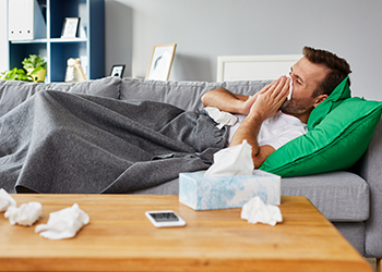 Sick man lying on sofa at home and blowing nose