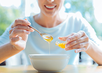 Smiling female adding honey to the porridge