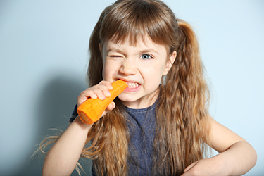 Little girl with carrot on wall background