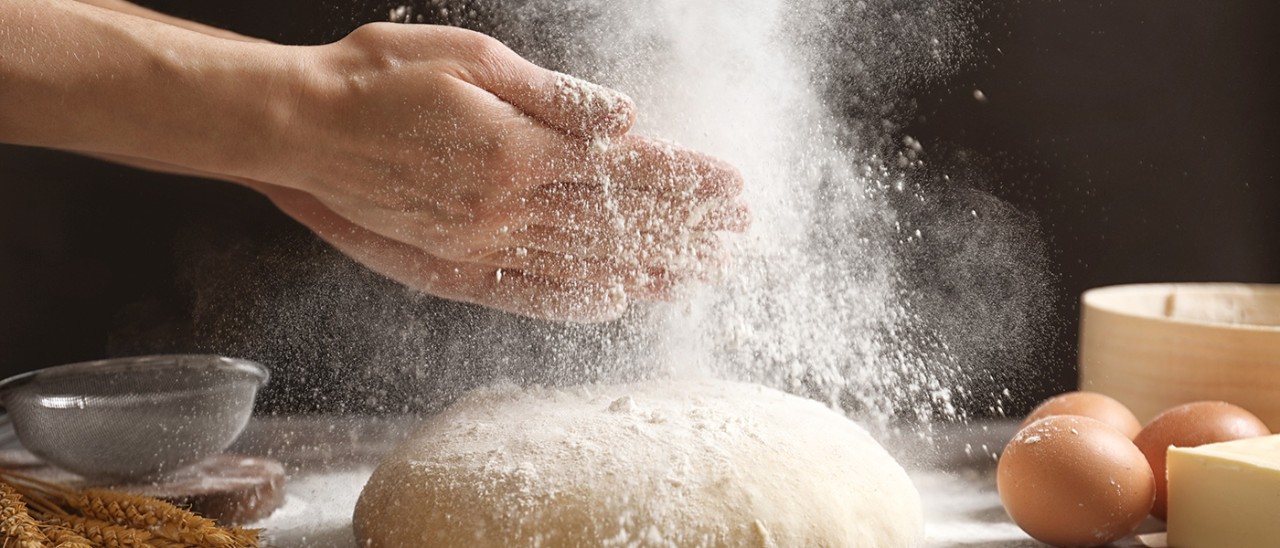 Woman clapping hands and sprinkling flour over fresh dough on table